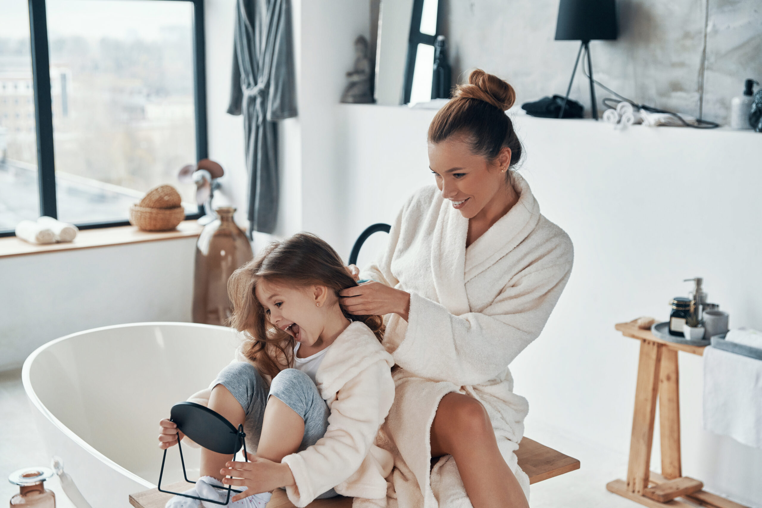 Beautiful young mother combining her daughter?s hair while doing